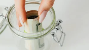 a women deposits rolled banknotes in a glass jar