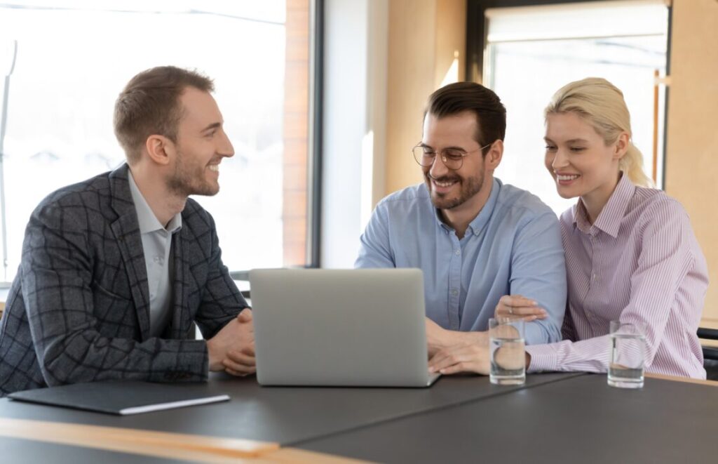 Three individuals collaborating with a laptop, emphasizing teamwork in brokerage.