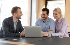 Three individuals collaborating with a laptop, emphasizing teamwork in brokerage.